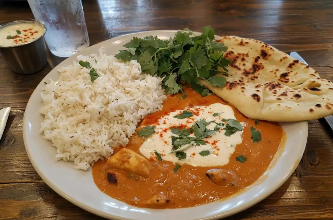 A plate of butter chicken with naan and rice on a rustic table